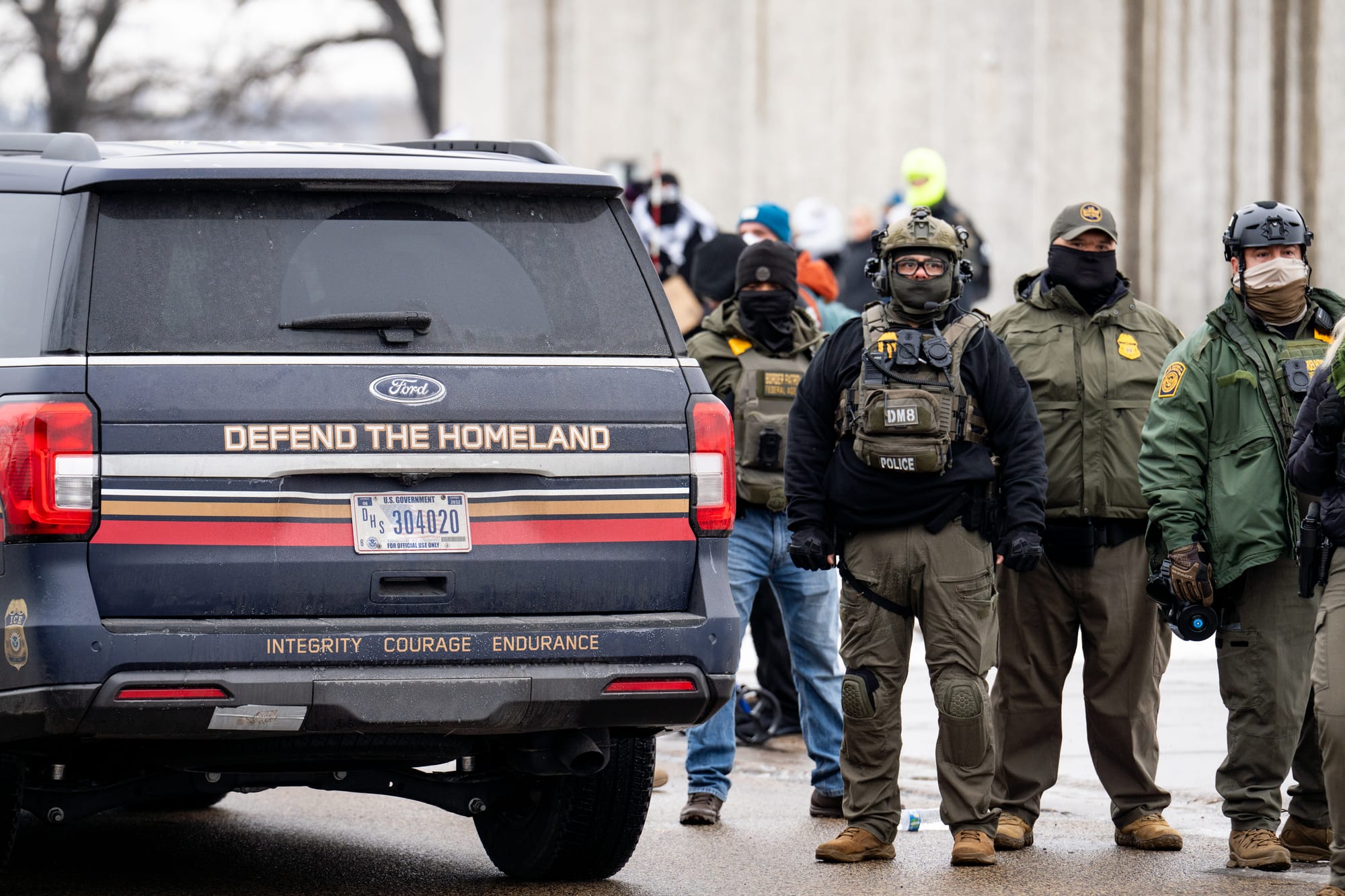 ICE/CBP agents in Minneapolis standing next to a Ford SUV with the slogan DEFEND THE HOMELAND on the bumper